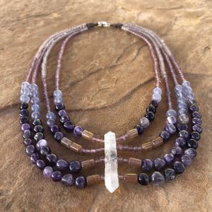 purple amethyst necklace with pink rutilated quartz, purple glass and clear quartz beads laying flat on a tan stone