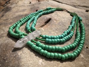 Green beaded necklace with a large double terminated quartz stone at the center, laying on a large rock in the sun. 