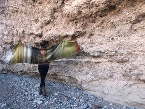 woman wearing a handwoven naturally dyed brown, green, yellow, grey, red and salmon shawl.