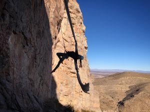 Woman doing aerial acrobatics off a cliff face with dramatic desert landscape. 