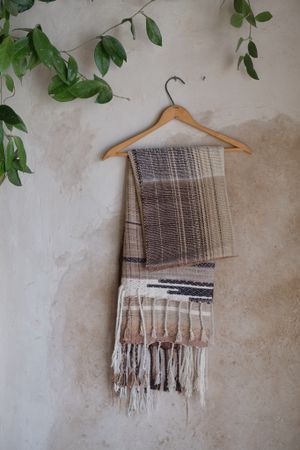 Black, tan & White handwoven merino Etherial Scarf hanging on a hanger on an adobe wall