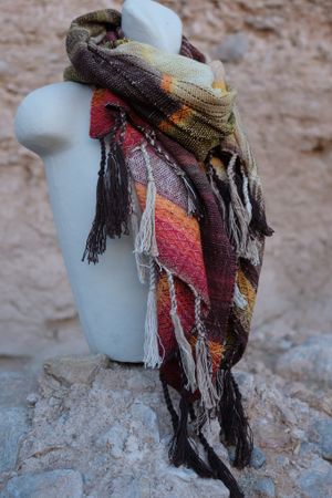 Handwoven red, orange, yellow, brown and white scarf on a white mannequin 