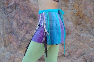 Woman wearing blue and purple fringed skirt with green leggings against a stone wall