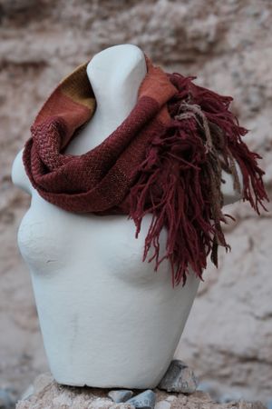 deep crimson red, orange, yellow and brown scarf on a white mannequin sitting on tan stones with an earthen tan background