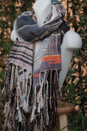 Handwoven raw silk etherial scarf in teal, blue, orange and dusty pink on a white mannequin in a garden