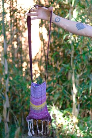 Simple Little Handwoven pink, yellow and purple raw silk Bag being held by an arm in front of bamboo