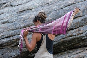 Woman wearing brown overalls and handwoven raspberry pink, brown and white scarf