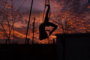 silhouette of a Woman doing a backbend on an aerial hoop with a dramatic orange pink sunset 