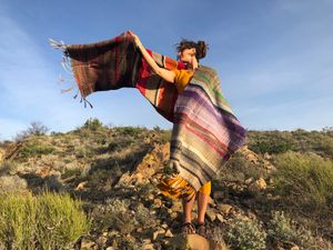 woman wearing Handwoven red, white, orange, green, purple, brown and black shawl standing in the desert