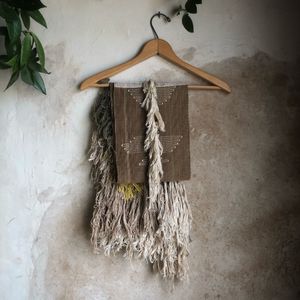 handwoven natural dye brown silk scarf with white, green and yellow fringe hanging on a hanger