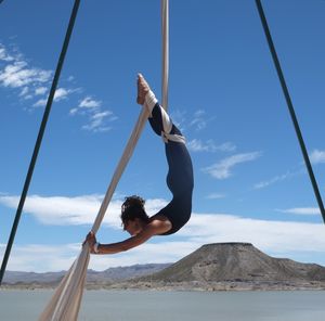 Woman hanging by her feet doing aerial silks in front of a dramatic desert landscape. 