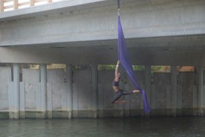 Woman doing aerial acrobatics with purple fabric, hanging from a bridge over the Rio Grande