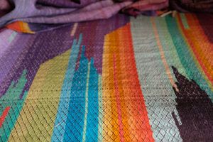 Brightly colored purple, blue, orange, green, black and pink handwoven fabric laying on a wooden floor. 