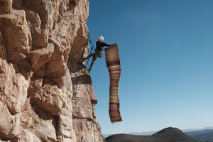 Woman holding large piece of handwoven fabric while hanging off a cliff in the desert