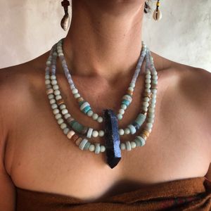 woman wearing three strand necklace made with a grey crystal point and blue-green beads 