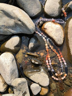 Detail of red-orange Botswanan agate, black tourmaline, purple fluorite necklace laying in the water of a creek