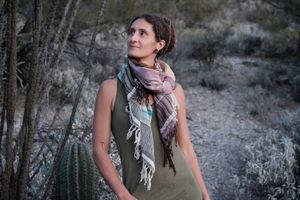 Woman wearing a blue, purple, white, brown and green scarf in the desert. 