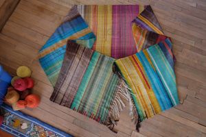 Handwoven textured diamond pattern fabric laying on a wooden floor, it is red, orange, blue, yellow, purple, brown and green