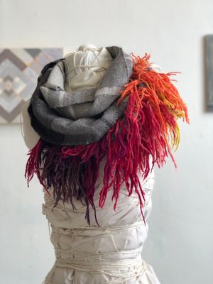 rainbow fringe, grey, black and white handwoven cowl scarf with fringe on a white mannequin in a white walled gallery