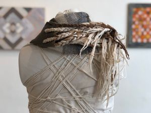 Brown, grey, black and white fringed and braided handwoven cowl scarf on a white mannequin in a gallery