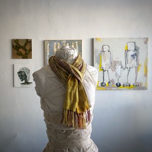 yellow scarf on a white mannequin in a gallery with paintings in the background