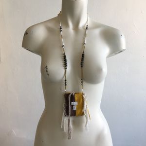 yellow brown and green beaded necklace with a brown and yellow woven pouch with white beadwork on a white mannequin