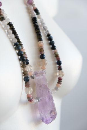 a white mannequin wearing a necklace with a purple amethyst centerpiece and stone beads in subtle shades of pink, grey, black