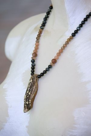 A white female form mannequin wears a necklace with a mokume pendant and stone beads of black and pale pink