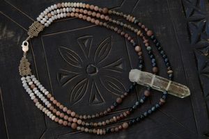 A black, pink and white necklace with a large citrine point at the center lays on a black wood surface 