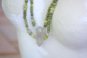 White female form mannequin wearing a crystal and green stone necklace 