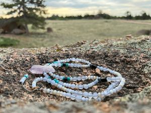 A purple amethyst, blue chalk, turquoise and black tourmaline necklace lays on a lichen covered rock