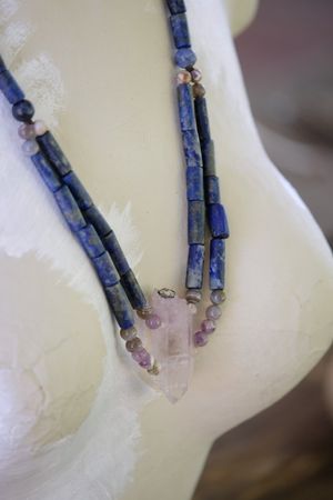 A blue lapiz and purple amethyst necklace rests on a white painted mannequin