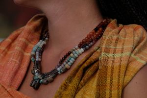 A woman wears a yellow, grey and orange diamond weave shawl with a beaded and knotwork necklace of many colors.  