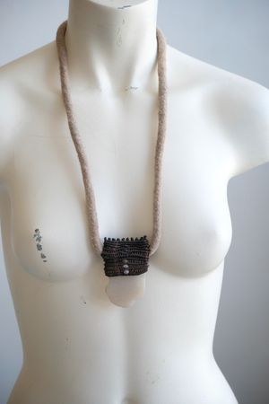 A white colored female form mannequin wears a sculptural necklace of a felted cord, dark purple basket
