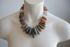 A white female form mannequin wears a sculptural necklace of ocean tumbled stones