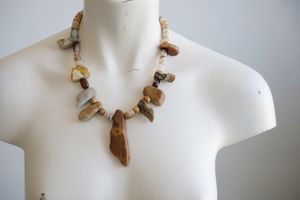 A white color female form mannequin wears a sculptural stone necklace in toffee, cream and yellow colors 