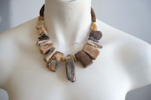 A white colored female form mannequin wears a sculptural necklace of petrified wood, stones, yellow glass beads and knot work