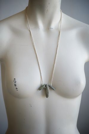 A white colored female form mannequin wears a sculptural necklace of white twined raw silk and three grey green stones