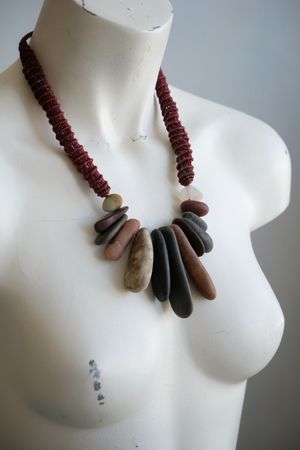 A white colored female form mannequin wears a sculptural necklace of multicolored smooth stones and knotwork