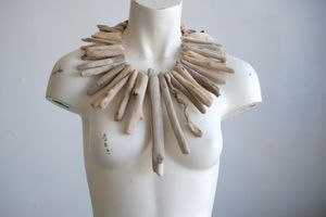A white female form mannequin wears a sculptural necklace of light colored drift wood