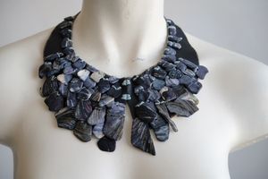 A white female formed mannequin wears a sculptural necklace of blue shells and blue leather