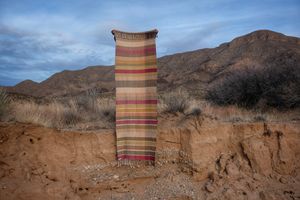 A detail of handwoven silk fabric in soft rainbow striped shades, naturally dyed, being held in a desert landscape