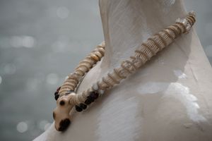 A white mannequin wears a white sculptural tubular knot work necklace with beads and a walrus tooth goddess at the center