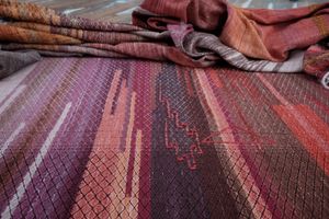 A detail of handwoven diamond pattern fabric in shades of red, pink and purple 