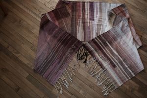 On a wooden floor rests handwoven fabric in shades of purple, mauve, burgundy and grey