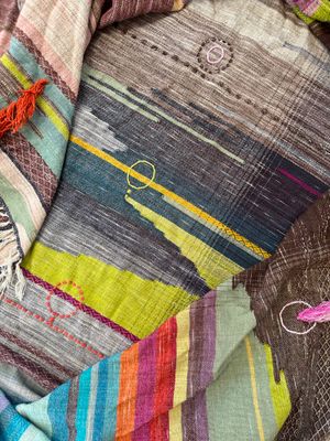A detail of raw silk handwoven fabric in a rainbow of hand dyed colors with circular moon-like details 
