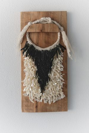 A handwoven sculptural necklace of black coral and mother of pearl hanging on a wooden frame