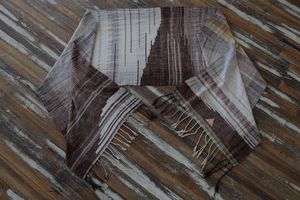 A large piece of handwoven fabric in shades of brown, cream and white rests on a dark wood floor