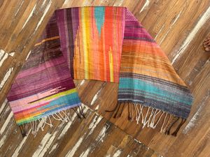 Handwoven fabric with a diamond pattern and vivid sunrise colors lays on a wooden floor