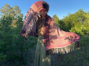 A woman wears a hand woven pink shawl in the forest